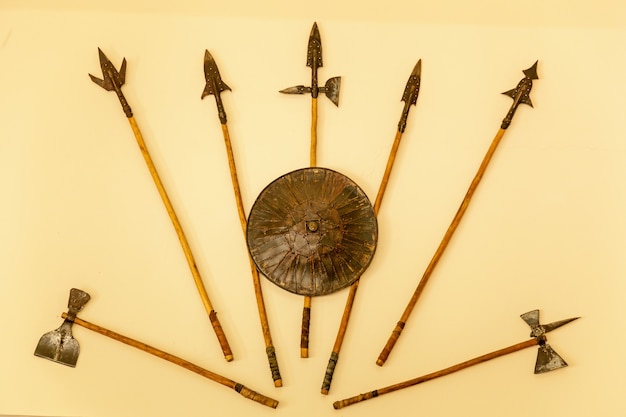 Photo a set of medieval weaponry. spears, axes, shield on beige background.