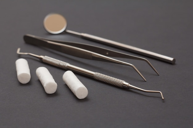 Set of metal dental instruments for dental treatment. Dental mirror, plugger, tweezers and cotton tampons on black background. Medical tools. Close-up view. Shallow depth of field.