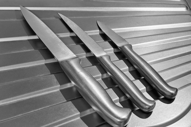 Set of metal kitchen knives on a chrome surface. Cooking concept. Black and white photo