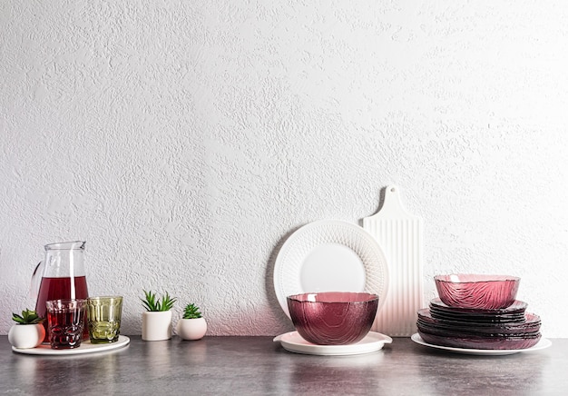 A set of modern glass burgundy dishes and a jug with grape juice on a stone countertop in the interior of the kitchen kitchen background