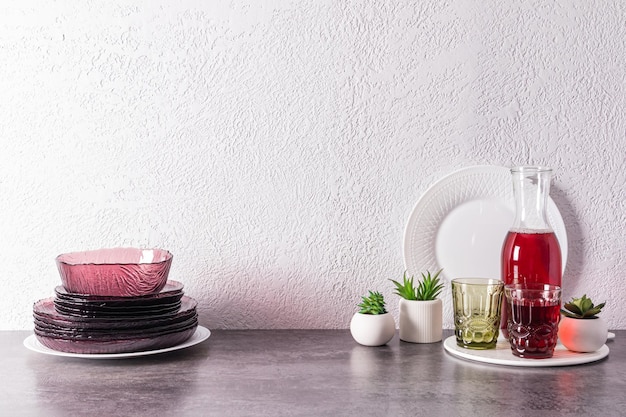 A set of modern glass burgundy dishes and a jug with grape juice on a stone countertop in the interior of the kitchen kitchen background