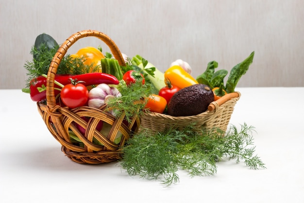 Set of multi-colored vegetables in two wicker baskets. Dill on table. Copy space. White background.