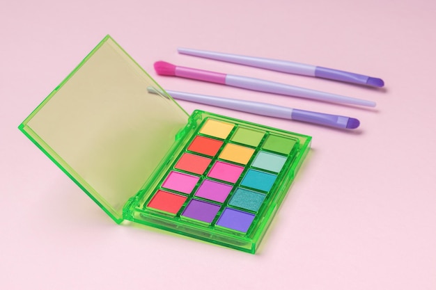 a set of multicolored eye shadows and brushes on a pink background
