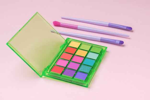 A set of multicolored eye shadows and brushes on a pink background