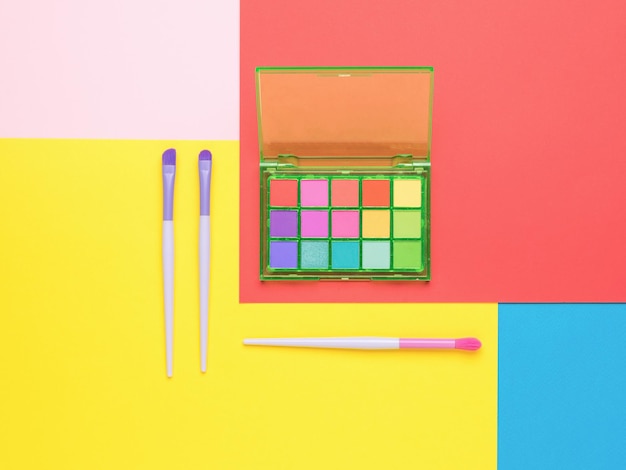 A set of multicolored eye shadows with brushes on a\
multicolored background flat lay