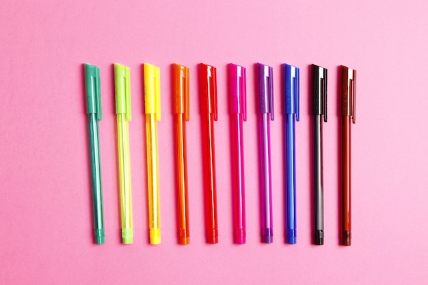 Set of multicolored pens on a pink background. Place for text. Top view.