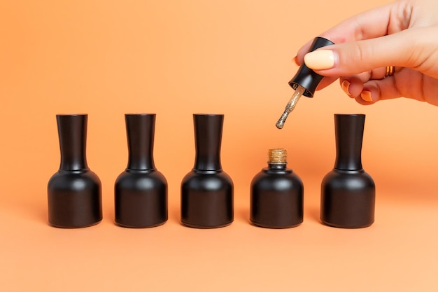 Set of nail polishes in black jars on a beige background female hand holds a brush for applying nail polish