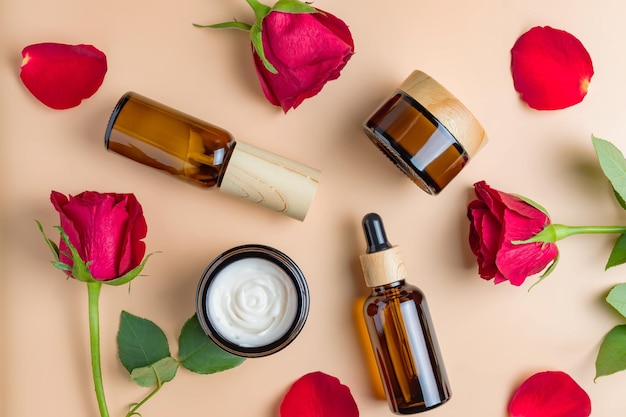 Set of natural organic spa beauty products on beige background\
with red roses and petals homemade rose face oil moisturizer cream\
jar amber glass spray bottle on beige background