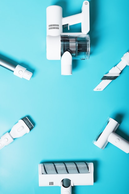 A set of nozzles and a white cordless vacuum cleaner in a row on a blue background