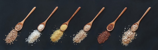 Набор различных злаков и риса в деревянной ложке на черном фоне, вид сверху