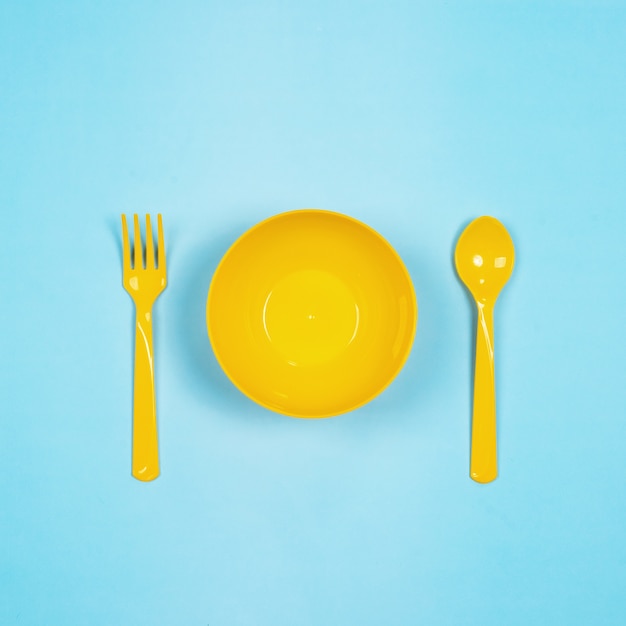Фото Набор пустых желтых пастельных пластиковых посуды миски, ложки и вилки