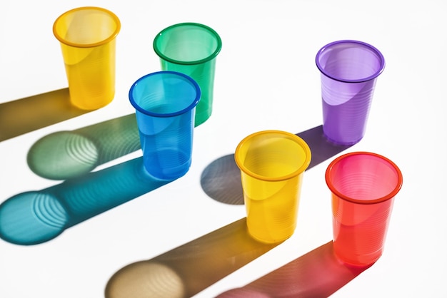 Фото Набор разноцветных пластиковых стаканчиков на белом фоне. длинные тени, студийный снимок.