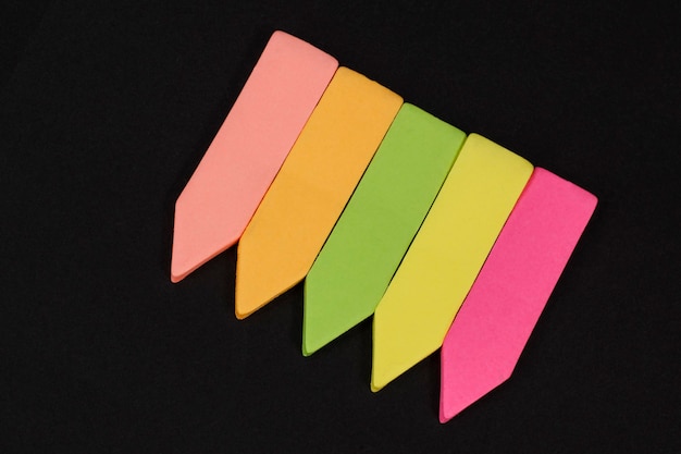Фото Набор разноцветных тонких бумажных офисных индексов с клеем на черном фоне.