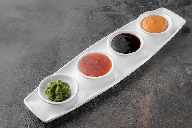 Фото Набор соусов для суши на белой тарелке васаби пряный сырный соевый темно-серый текстурированный фон вид сбоку