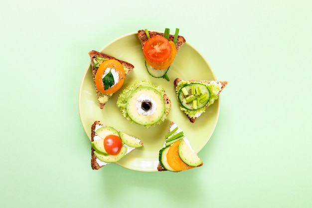 Фото Набор вегетарианские бутерброды на круглой зеленой тарелке на зеленом фоне.