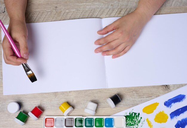 Фото Набор акварельных красок, кистей и бумаги с различными штрихами и цветами женские руки, держащие