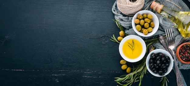 A set of olives and olive oil and rosemary Green olives and black olives On a black wooden background Free space for text