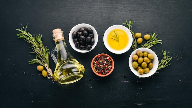 Un insieme di olive e olio d'oliva e rosmarino olive verdi e olive nere su uno sfondo di legno nero spazio libero per il testo