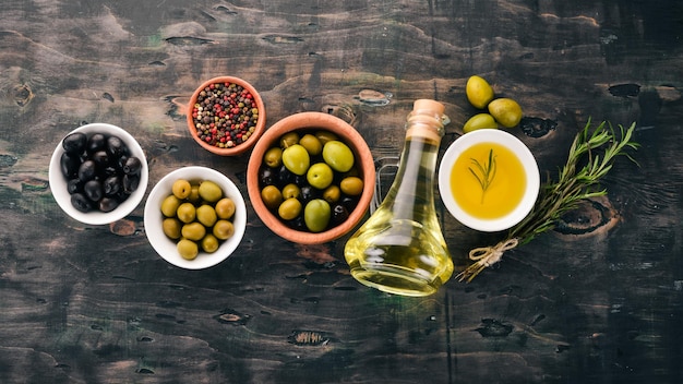 A set of olives and olive oil and rosemary Green olives and black olives On a black wooden background Free space for text