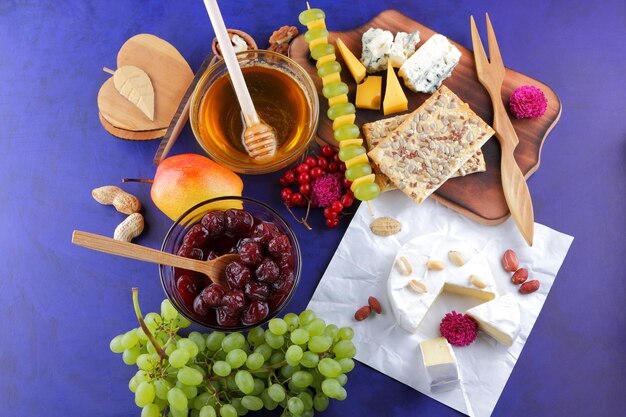 Фото Набор или ассортимент сыров крупным планом различные виды сыров с орехами, ягодами, фруктами, вишневым джемом и медом на синем фоне