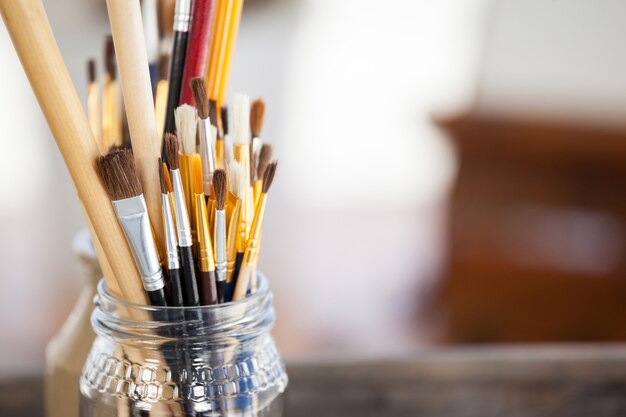 Set of paint brushes in a jar on wooden table