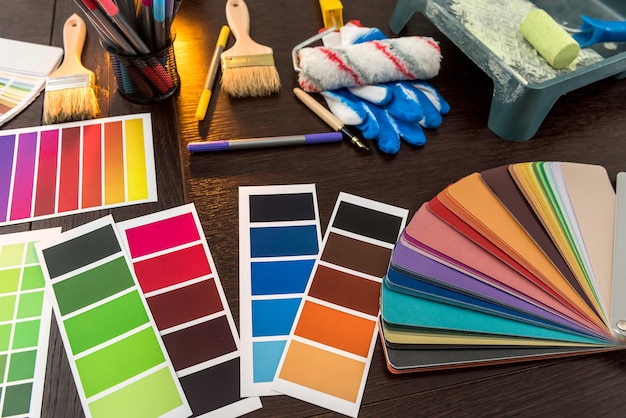 set of paint brushes roller tray and colour paper palette on wooden board