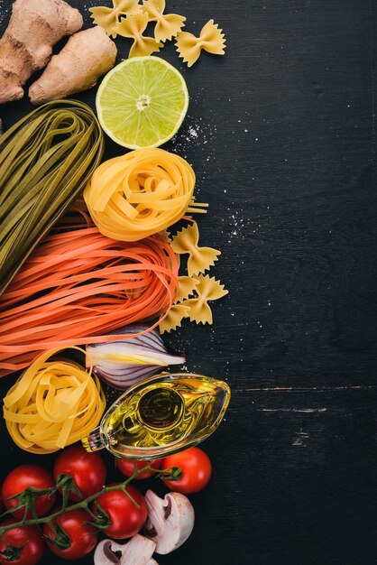 パスタヌードルのセットスパゲッティタリアテッレフェットチーネファルファッレイタリア料理新鮮な野菜とスパイス黒い木製の背景に上面図コピースペース