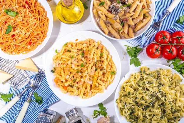 Set of pasta with different sauces on white tiled background Spaghetti farfalle penne fusilli pasta with seafood spinach carbonara tomato sauce Italian dinner Mediterranean food concept