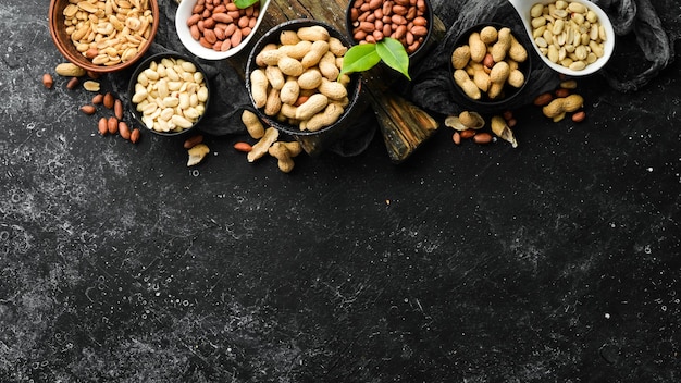 Set of peanuts in bowls on a black stone background Nut background Top view