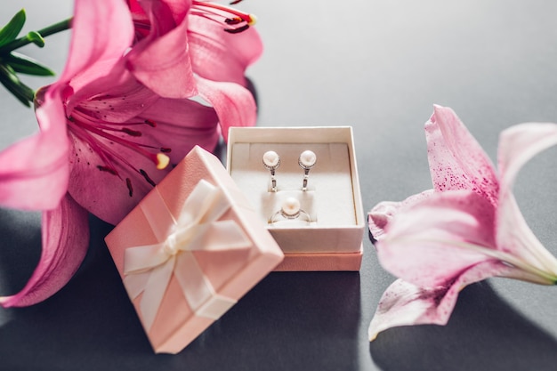 Set of pearl jewellery in pink gift box with flowers Silver earrings and ring with lily on grey background