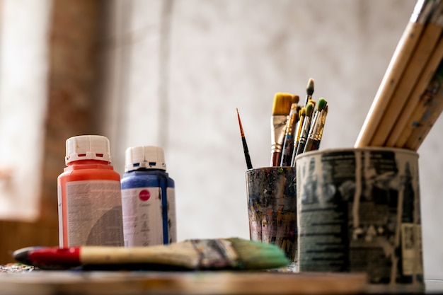 Set penselen in blikken en twee plastic potjes met rode en blauwe gouache op werkplaats van schilder