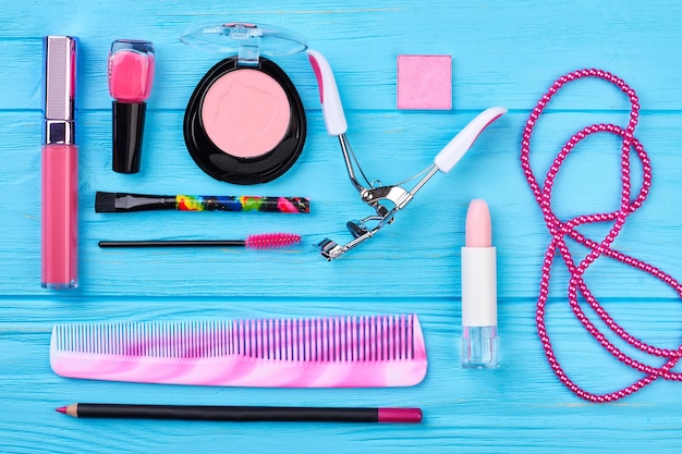 Set of pink cosmetics and accessories. women makeup products\
and tools, blue wooden background. beauty items for fashion\
look.