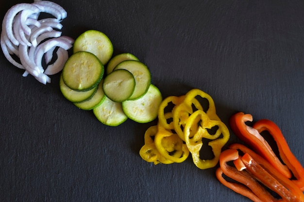 Set plakjes groenten (peper, ui, courgette) geïsoleerd op zwarte achtergrond. Bovenaanzicht