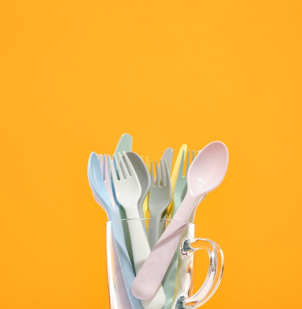 Set of plastic tableware in light colors in a glass cup on the table Spoons forks and knives Space for text