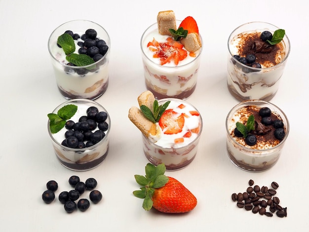 Set of portioned desserts in a glass of mascarpone or ricotta with savoiardi biscuits and berries