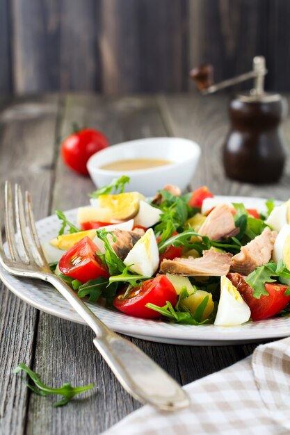 Set of raw ingredients potatoes, eggs, fresh arugula, olive oil, pepper, canned tuna, cherry tomatoes, salt to prepare a salad Nicoise on the old wooden background. Rustic style.Selective focus.