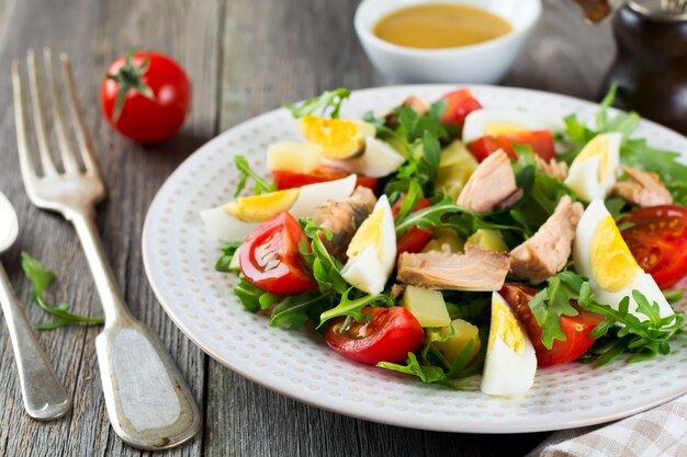 Set of raw ingredients potatoes, eggs, fresh arugula, olive oil, pepper, canned tuna, cherry tomatoes, salt to prepare a salad Nicoise on the old wooden surface