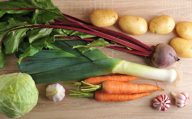 Set of raw vegetables for healthy eating, leek, beets, potatoes, carrots, cabbage, garlic on a wooden background