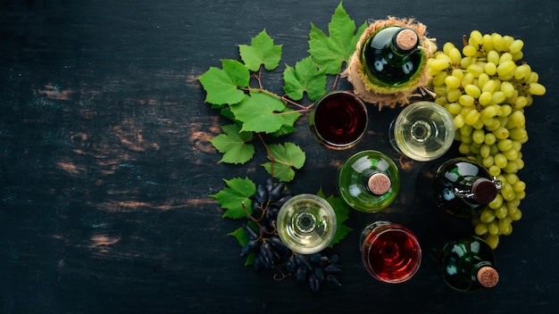 Набор красного и белого вина в бутылках и бокалах Виноград на черном деревянном фоне Свободное место для текста Вид сверху