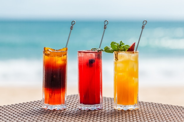 Набор освежающих фруктовых коктейлей, стоящих на столе на пляже у бирюзового моря