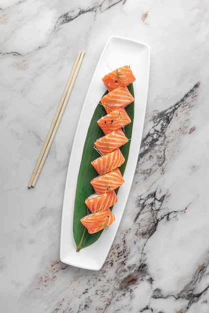 Photo set of rolls philadelphia kappa with microgreens and green bamboo leaf in a white ceramic plate with chopstick on a bright textured marble background top view