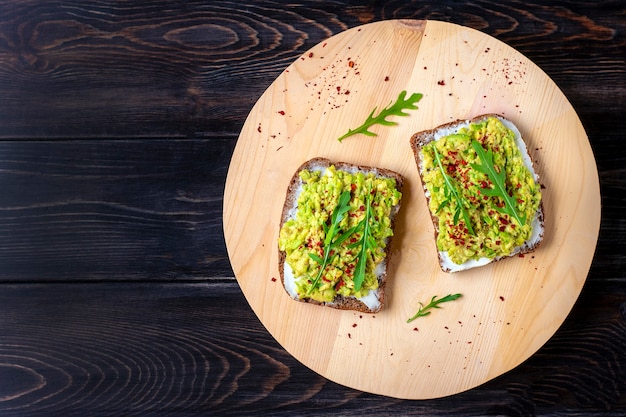 Set sandwiches for breakfast - slice of whole grain dark bread, guacamole on wooden table