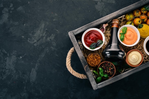 Set of sauces Ketchup mayonnaise mustard soy sauce barbecue sauce pepper and spices On a black stone background Top view Free space for text