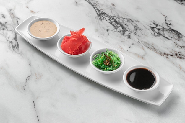 Set sauzen voor sushi op een witte plaat gember soja sesam zeewier heldere getextureerde marmeren achtergrond zijaanzicht