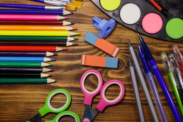 Set of school stationery supplies. Colored pencils, watercolor paints, paintbrushes, pens, scissors, eraser, sharpener on wooden desk. Back to school concept