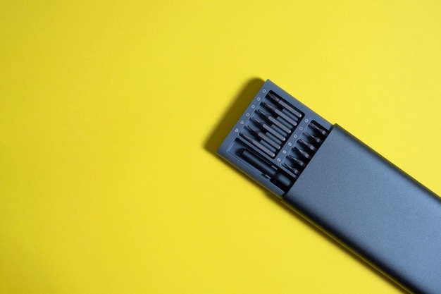 A set of screwdrivers with bits in a case on a yellow background. Copyspace, tools for work