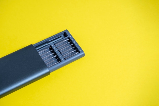 A set of screwdrivers with bits in a case on a yellow background. Copyspace, tools for work