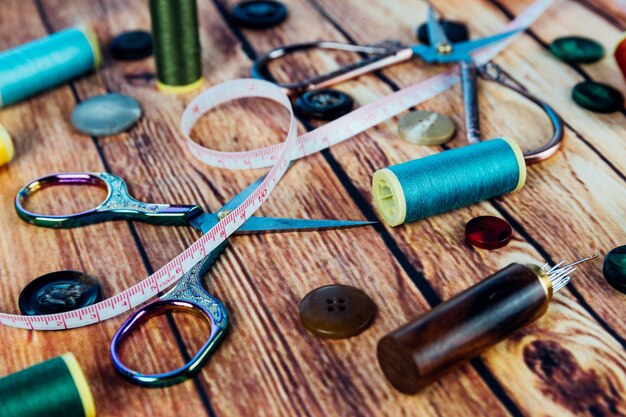 Set of sewing accessories such as spools of colored thread, buttons, measuring tape, vintage scissors and sewing needles on wooden background