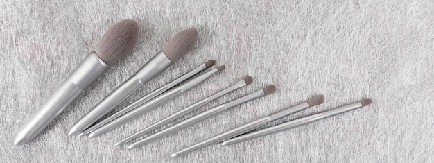 Set of silver color professional makeup brushes on gray colored background Creative concept of beauty Banner Copy space Flat lay