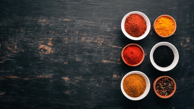 A set of spices and herbs Indian cuisine Pepper salt paprika basil turmeric On a black wooden chalkboard Top view Free copy space